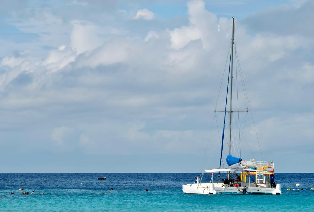 A catamaran floats on turquoise Caribbean sea under a cloudy sky in Barbados.